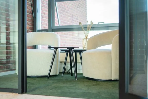 Twee moderne fauteuils met ronde vormen en een set zwarte bijzettafels in een zithoek aan de Joop Geesinkweg.